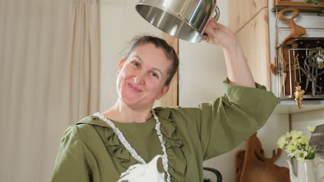 cook playfully holds electric mixer coated with thick whipped dough and lifts empty bowl upside down above head to show stickiness of mixture while smiling joyfully in cozy kitchen environment