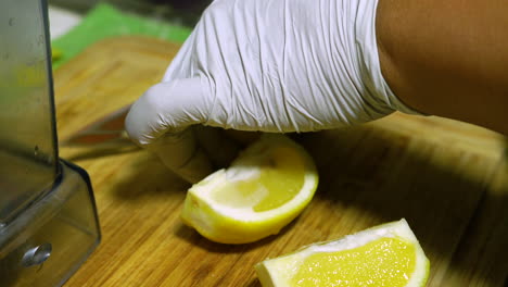 a person wearing white gloves is cutting a lemon on a bamboo cutting board