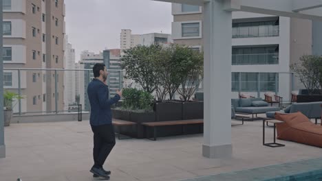 executive man talking on the phone while walking along the rooftop terrace of a modern building. pan right following the man.