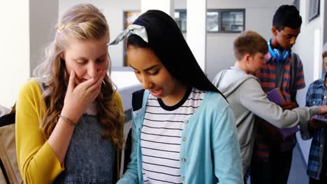 Smiling-schoolgirls-using-mobile-phone-in-corridor