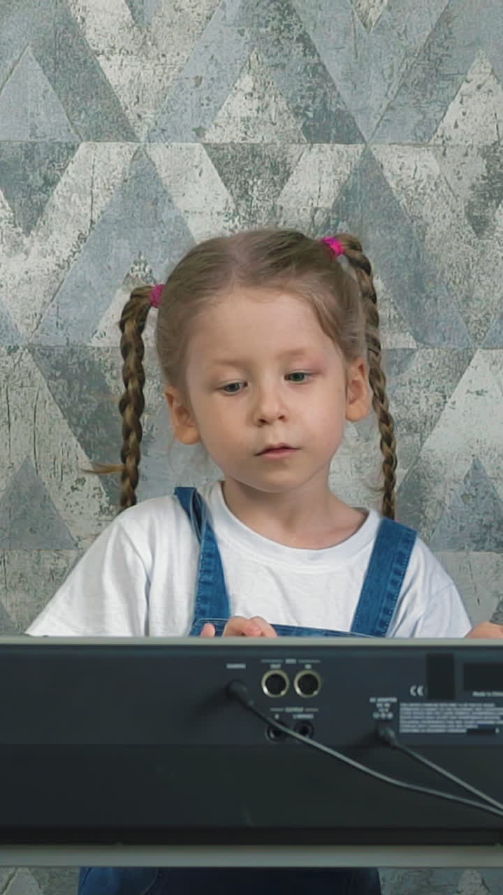 slow motion little girl with long pigtails plays on electronic piano at home, in self-isolation and quarantine mode, sad ballad