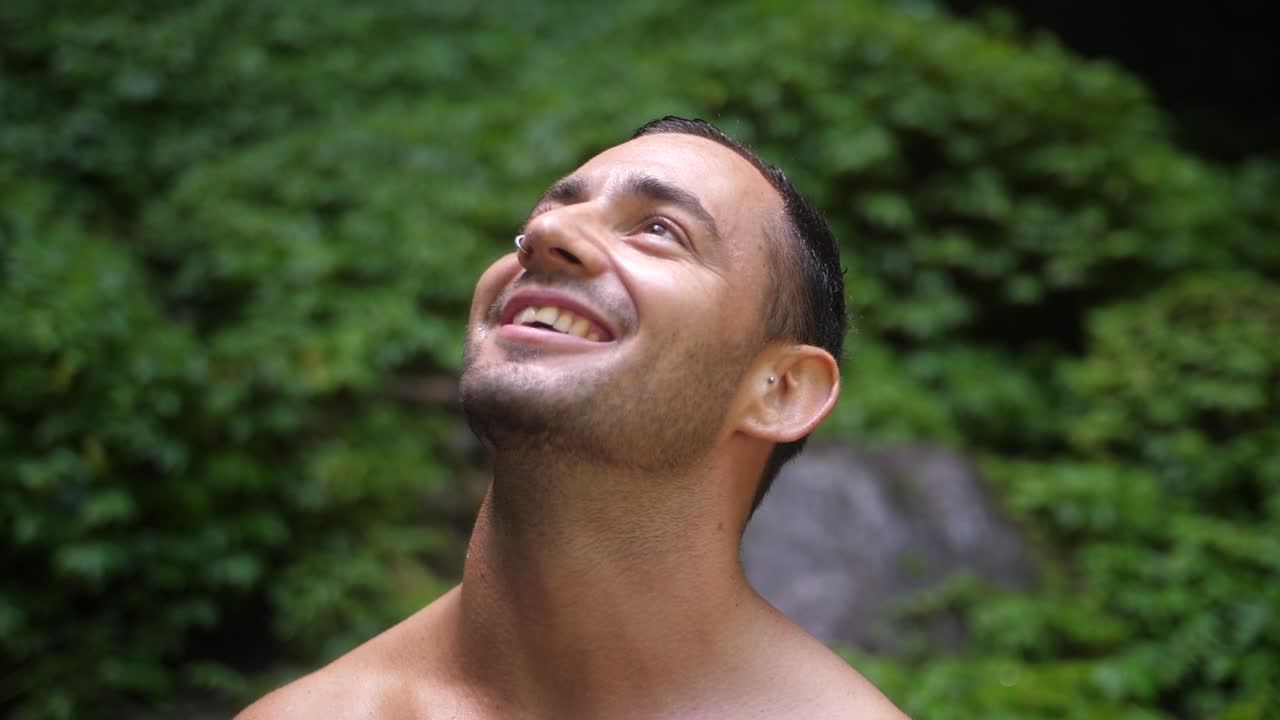 Un uomo giovane e attraente con un'espressione felice e gioiosa, che guarda nell'obiettivo e si guarda intorno nella giungla lussureggiante e verde di Bali mentre sorride