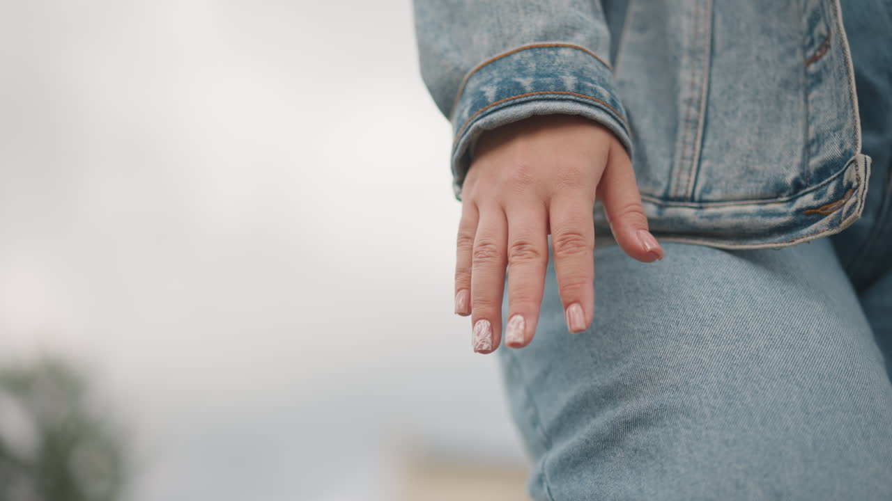 Jeans jacket hand lowangle walk, cinematic closeup of person striding with poise, textured denim, manicured nails, cloudy backdrop, fashionforward editorial atmosphere, confident movement