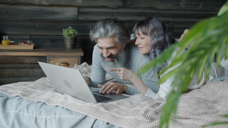 couple relaxing on bed, using laptop