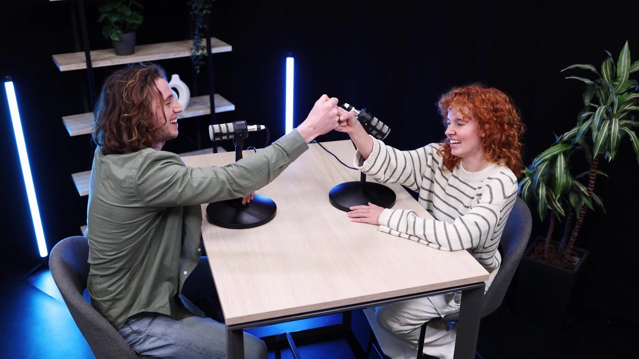 Glada unga man och kvinna spelar in en podcast i en modern studio.