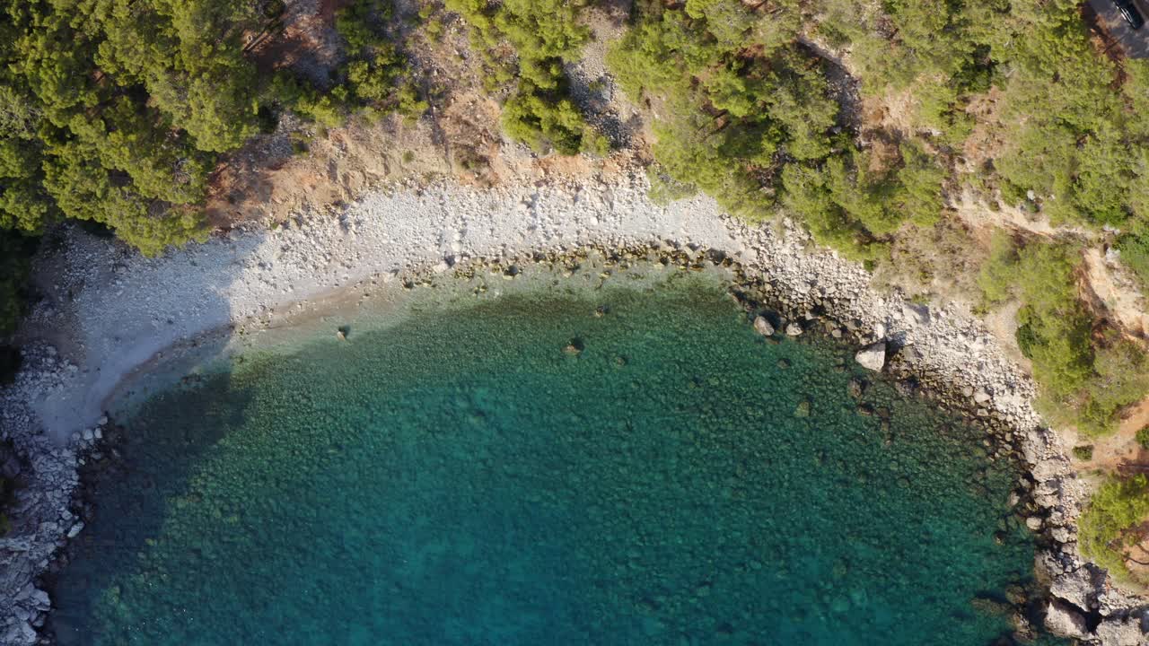 Slow upward crane motion above scenic Turkish cyan green water bay in sunlight