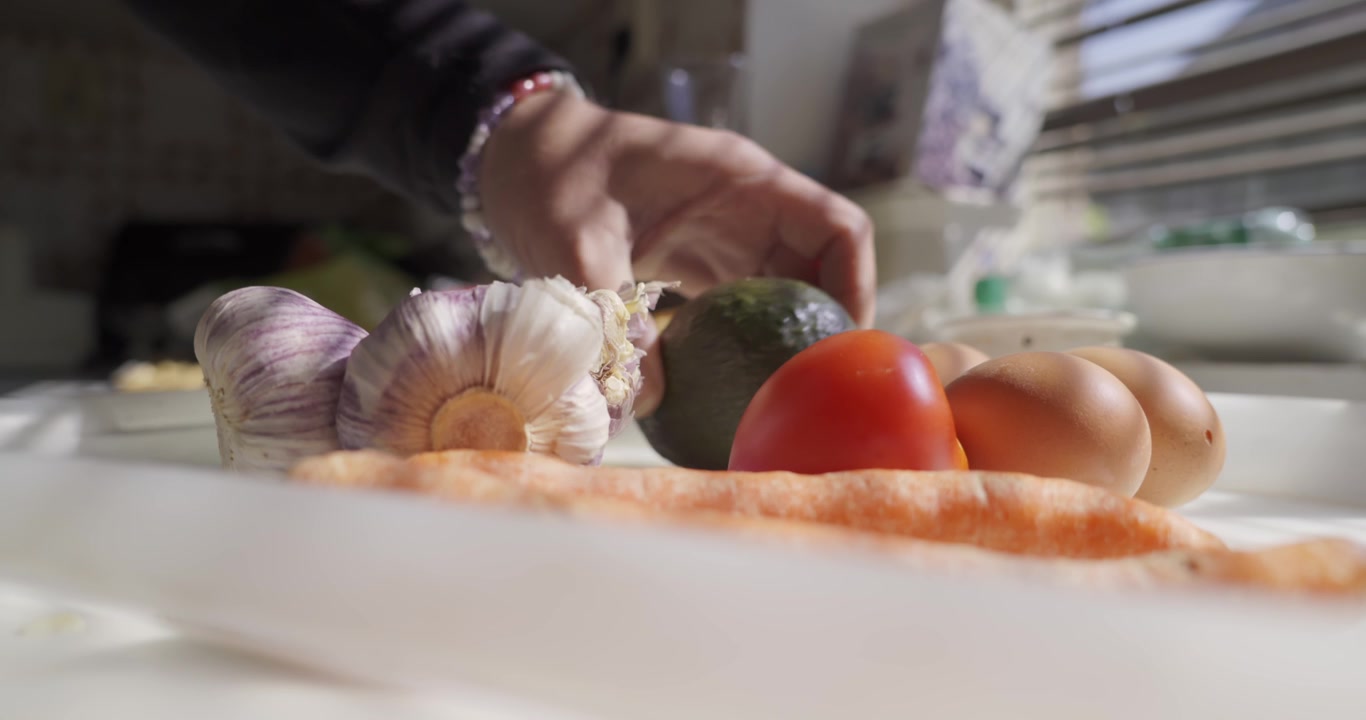 A person's hands place garlic, eggs, carrots and a tomato on a white tray in the morning sun and then take it out of the frame