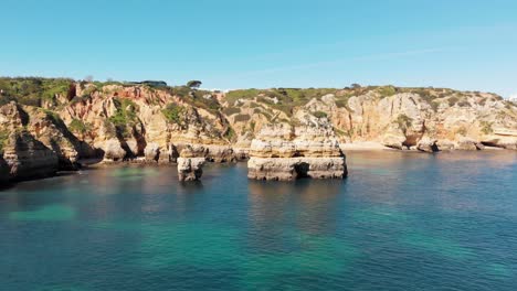 Barren-eroded-scraps-of-land-standing-amidst-Turquoise-Algarve-Sea-in-Lagos,-Portugal---Aerial-eye-level-slide-shot