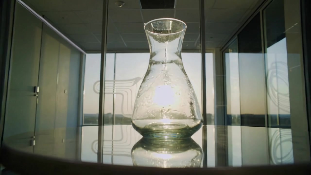 Shining low sun shifting across horizon, altering carafe reflection on glass table in meeting room