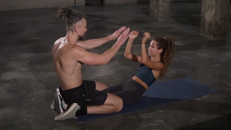 Young-stylish-people-sporty-man-and-woman-are-doing-situps-and-clapping-hands-training-together-at-loft-studio-enjoying-pair-work.-Youth,-healthy-lifestyle-and-relationship-concept