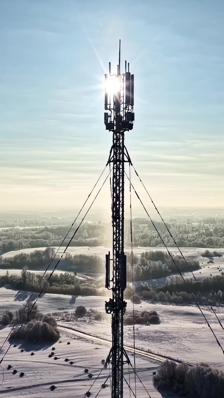 Ripresa aerea cinematografica di una torre cellulare 5G che si erge su un paesaggio invernale ghiacciato con bagliore solare. Utile per concetti di telecomunicazioni, connettività internet e tecnologia remota.