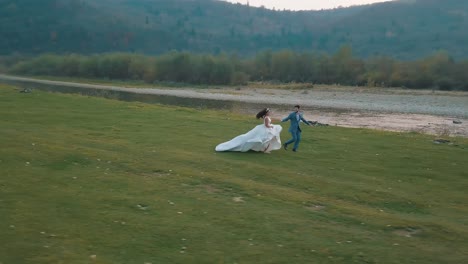 Wedding-couple-running-near-mountain-river.-Groom-and-bride.-Arial-view