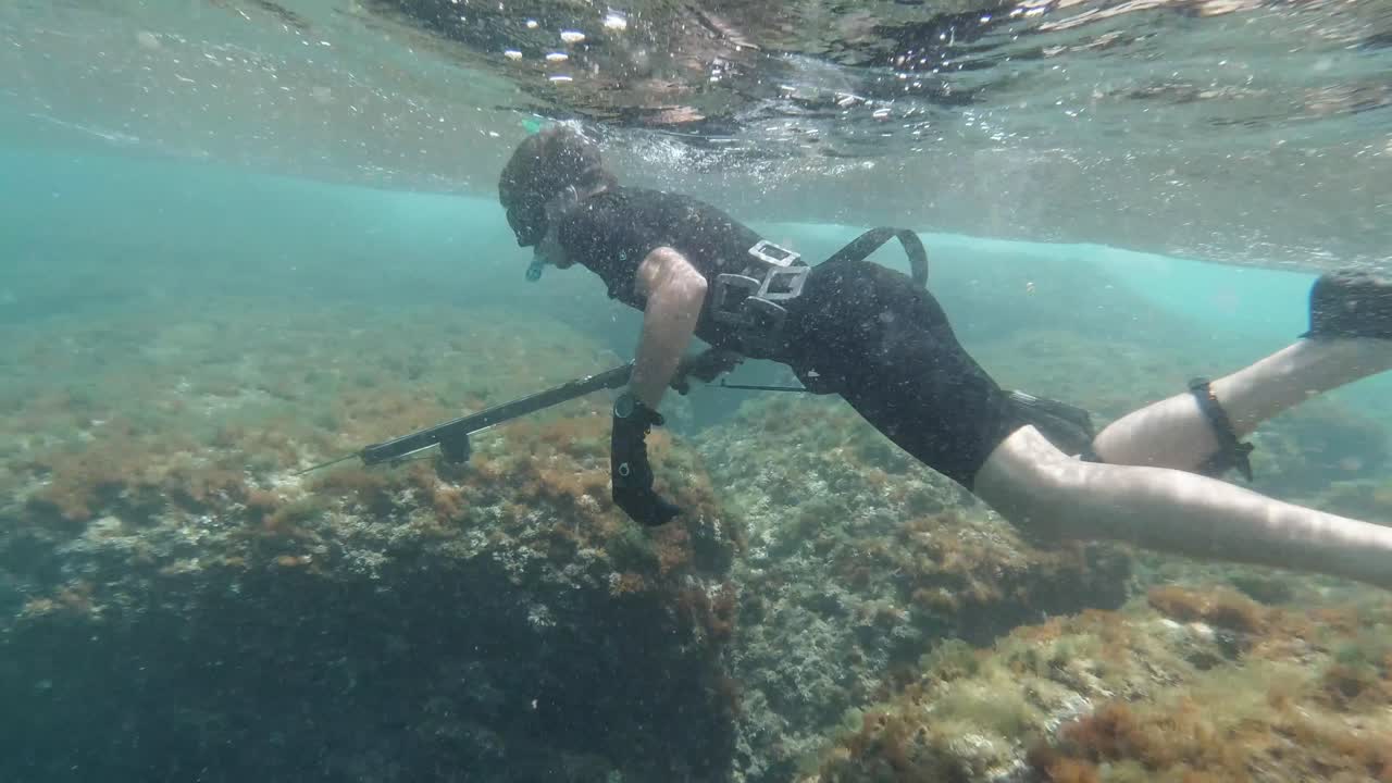 Spearfisher snorkelling in shallow water looking for fish in slow motion