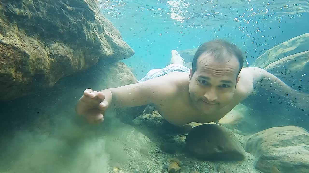 joven sosteniendo la respiración en agua azul clara en el día desde el ángulo frontal