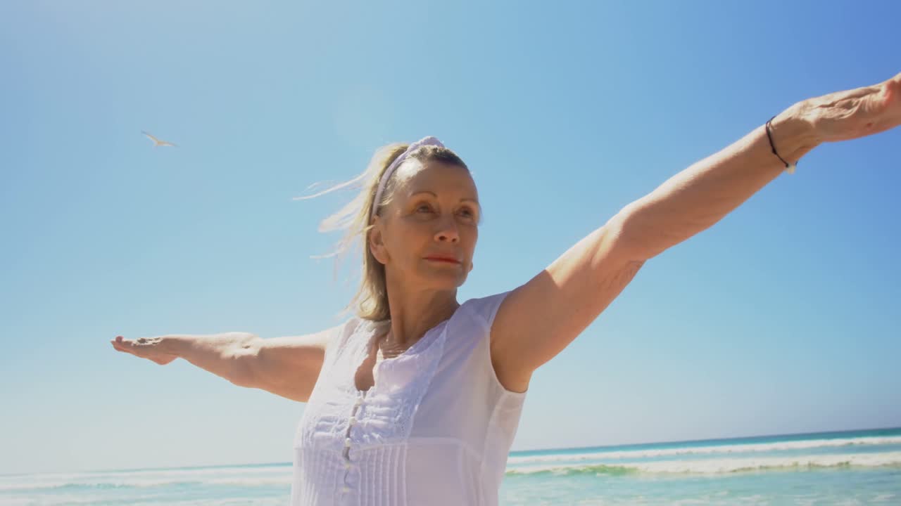 vista frontal de una mujer caucásica senior activa realizando yoga en la playa 4k