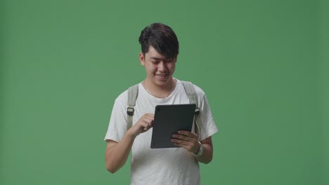 asian man student using tablet and walking on green screen studio