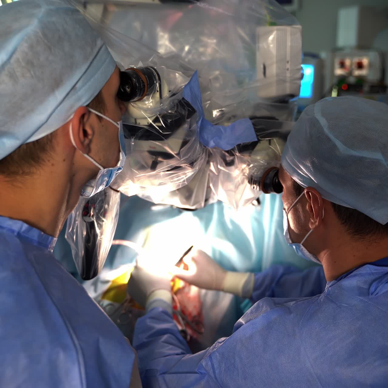 Male surgeons using the microscopes to perform the operation. The place of operation in blur. Doctors close up