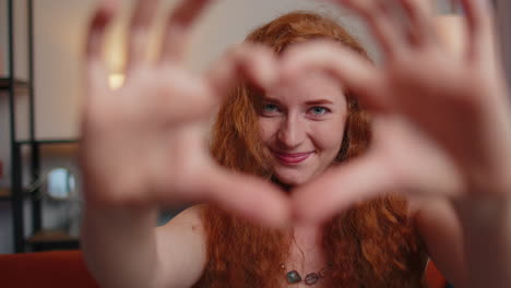 redhead young woman makes symbol of love, showing heart sign to camera, express romantic feelings