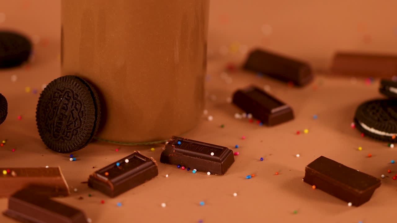 Chocolate milkshake with whipped cream, sprinkles, chocolate bar, on brown background, smooth camera push