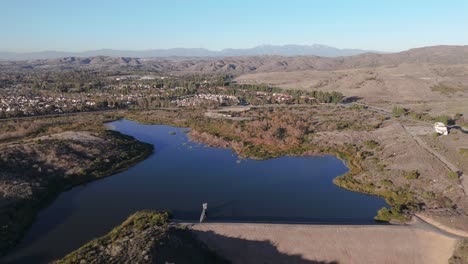 circling shot of lake with dam surrounded by hiking trail and suburbs