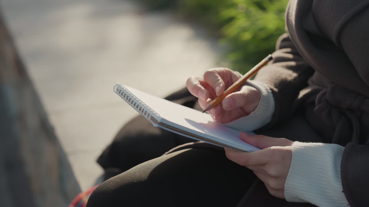 Annota idee in un ambiente esterno sereno. Impegnata in scrittura riflessiva sotto il sole del parco. Cattura pensieri creativi seduta su una panchina in un contesto naturale e tranquillo.