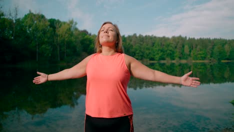 A-woman-in-sportswear-near-a-lake-with-open-arms-in-the-air