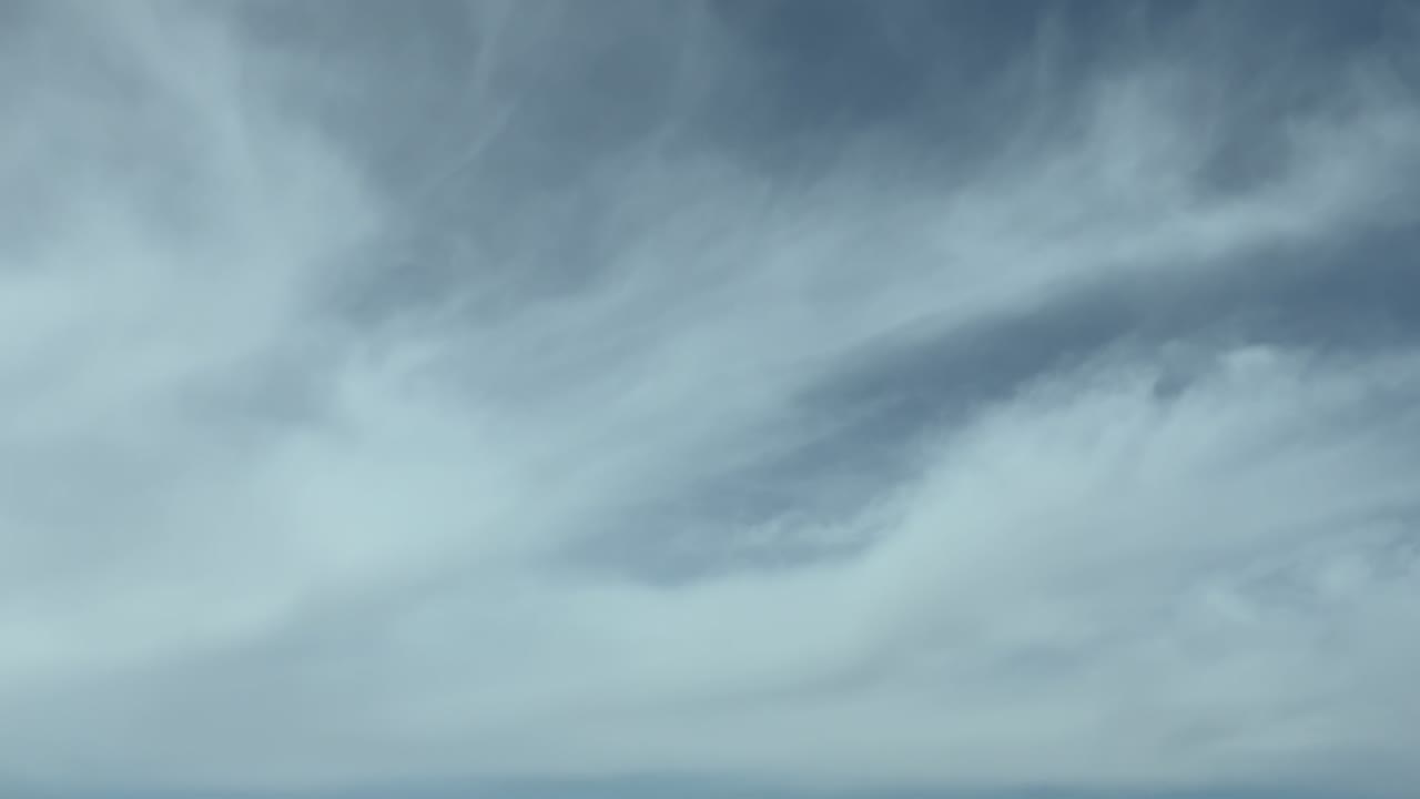 An aerial POV flying through ethereal and vaporous frayed clouds under a blue sky; footge taken from inside an airplane cockpit.