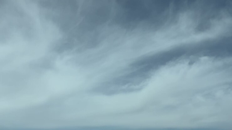 An aerial POV flying through ethereal and vaporous frayed clouds under a blue sky; footge taken from inside an airplane cockpit.