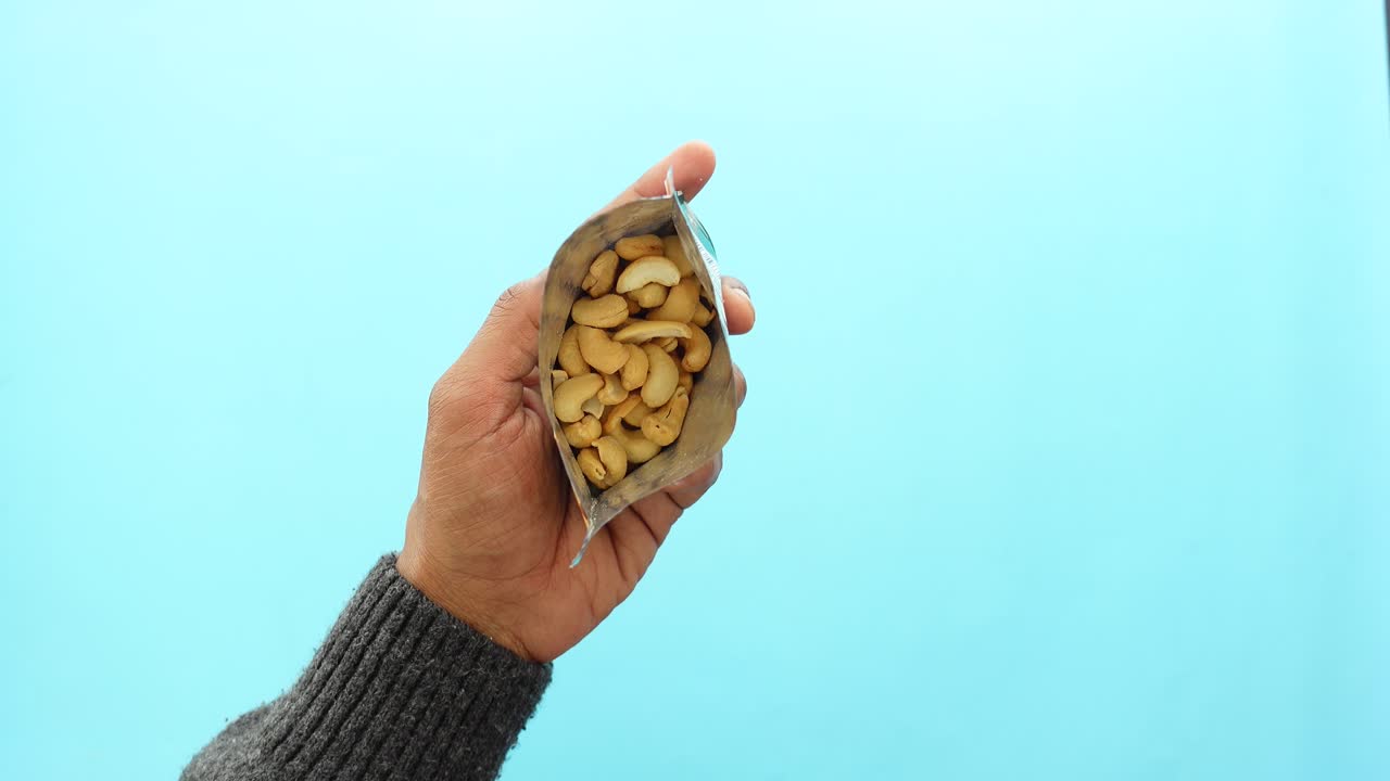 A person holding an open packet of cashews