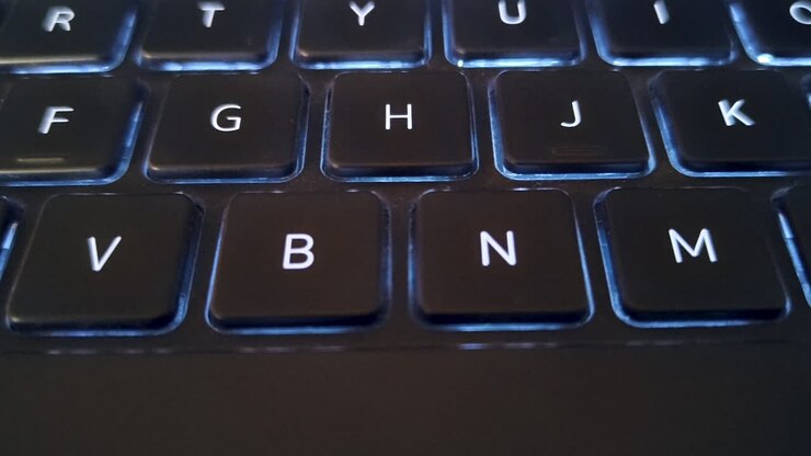 Macro primo piano di tastiera di laptop con retroilluminazione blu in condizioni di scarsa illuminazione, ideale per la programmazione, la cybersecurity, il lavoro da casa, contenuti tecnologici e immagini di stile di vita digitale