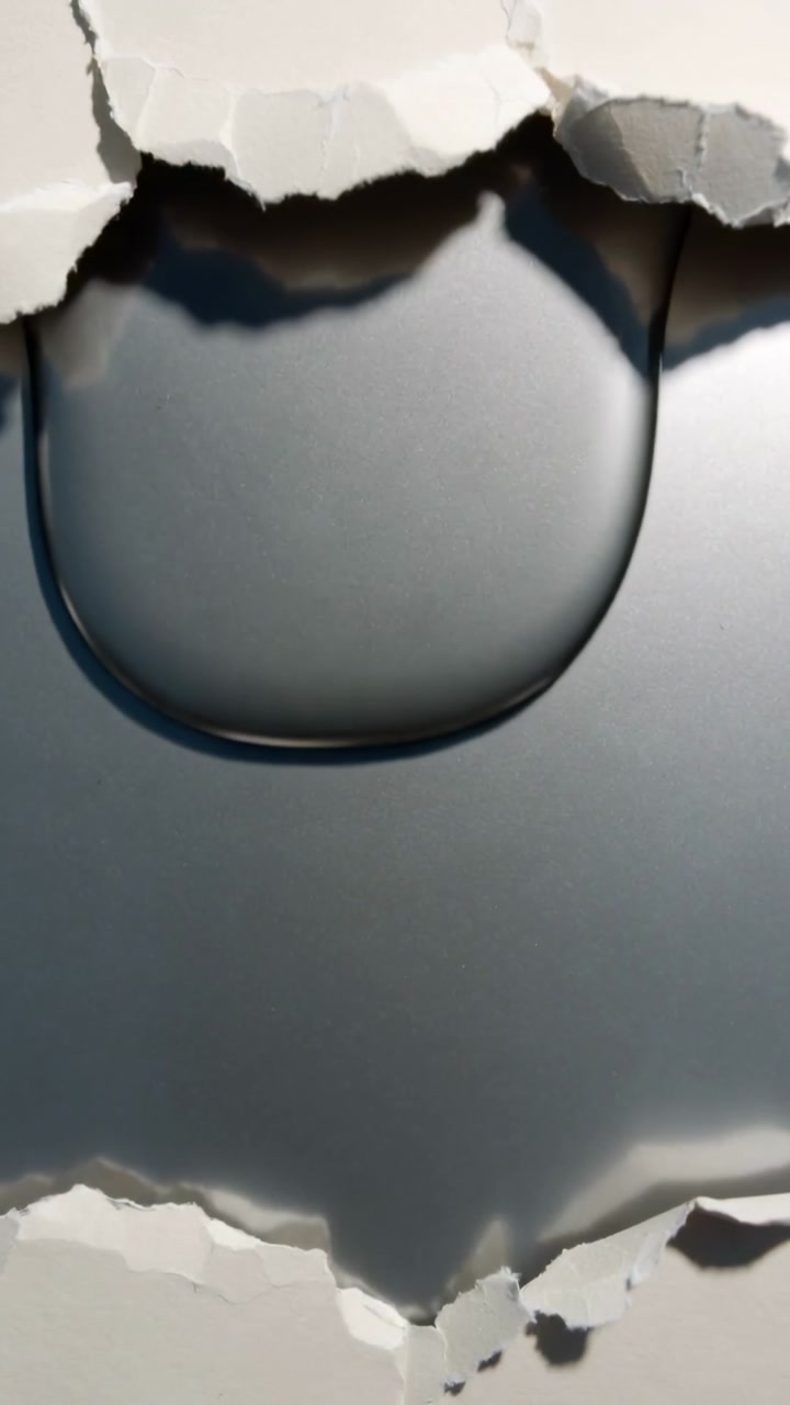 Vertical video: Forming clear droplet at upper torn rim over dark backing in studio gravity pulling