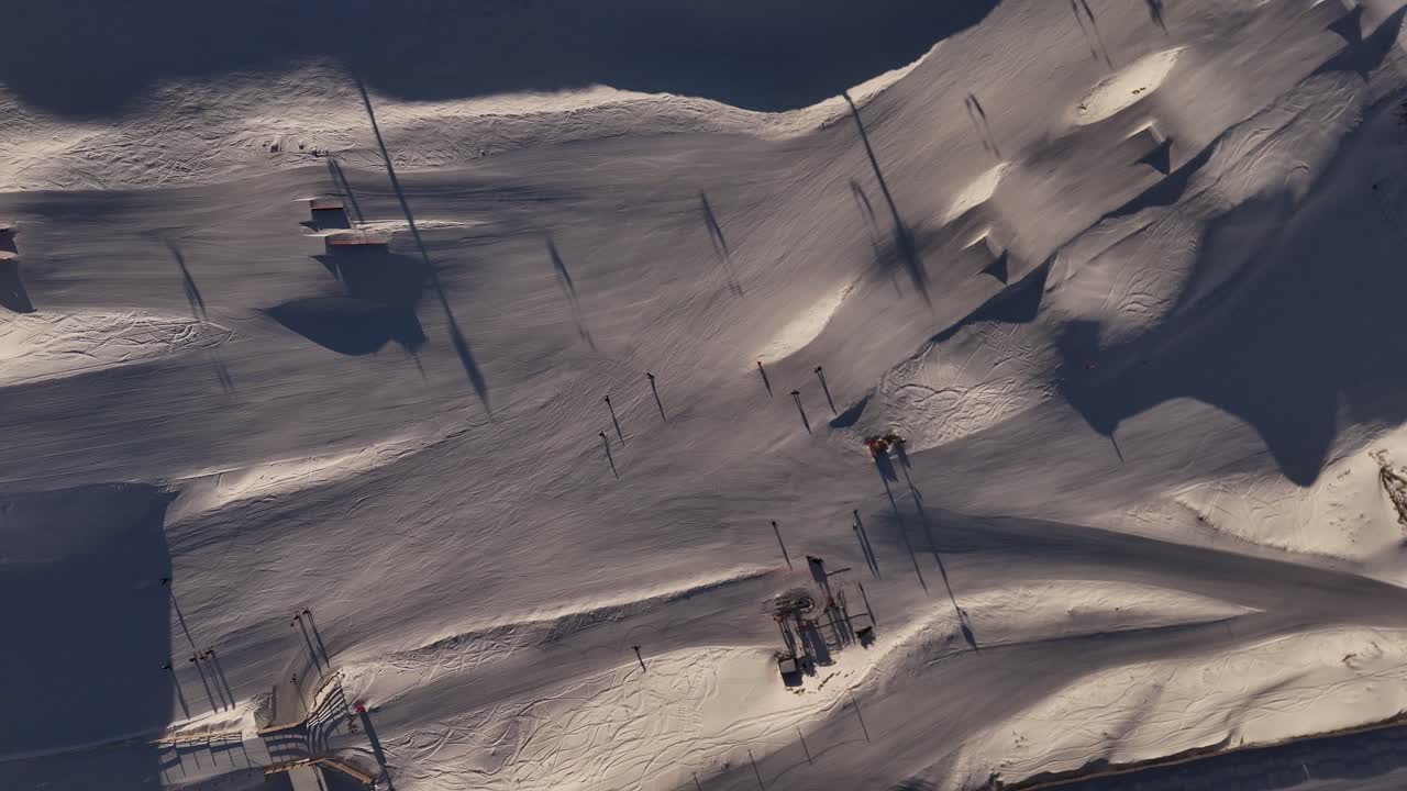 Stunning 4K 60fps aerial top-down footage of skiers on the slopes of Cardrona Ski Resort in New Zealand. Shot at sunrise, capturing the beautiful morning light on the snowy mountain landscape