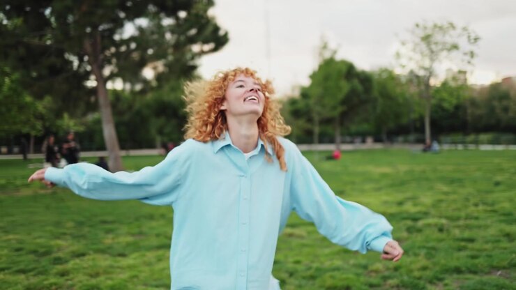 Giovane donna felice con capelli rossi ricci che balla in un parco.