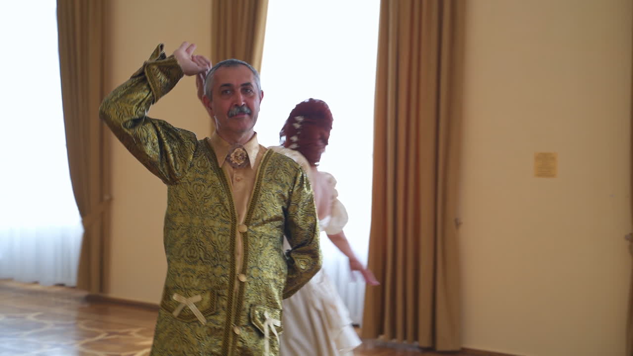 Aging couple in historic outfits performing a dance. Adult people in a big dance ballroom of a castle.