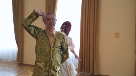 aging couple in historic outfits performing a dance. adult people in a big dance ballroom of a castle.