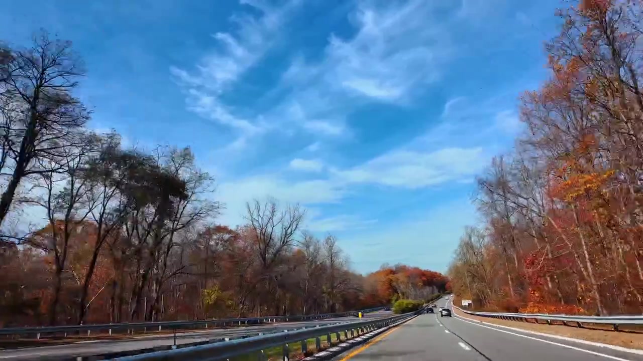 Strada autostradale con cartello di benvenuto a New York in autunno. Strada asfaltata con segnali stradali e alberi con fogliame autunnale sotto un cielo blu con nuvole sottili mentre si entra a New York.