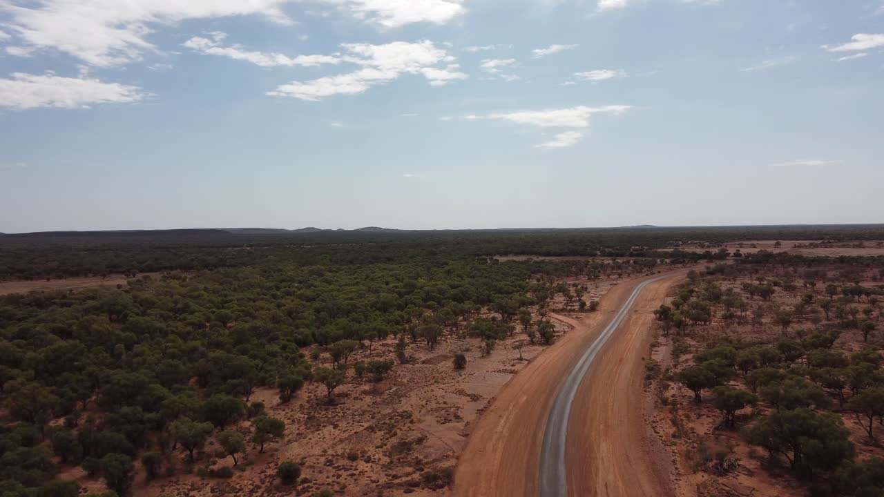Avustralya taşrasında kırmızı toprak ve ağaçlarla çevrili, çok uzak bir kırsal yol üzerinde uçan drone.