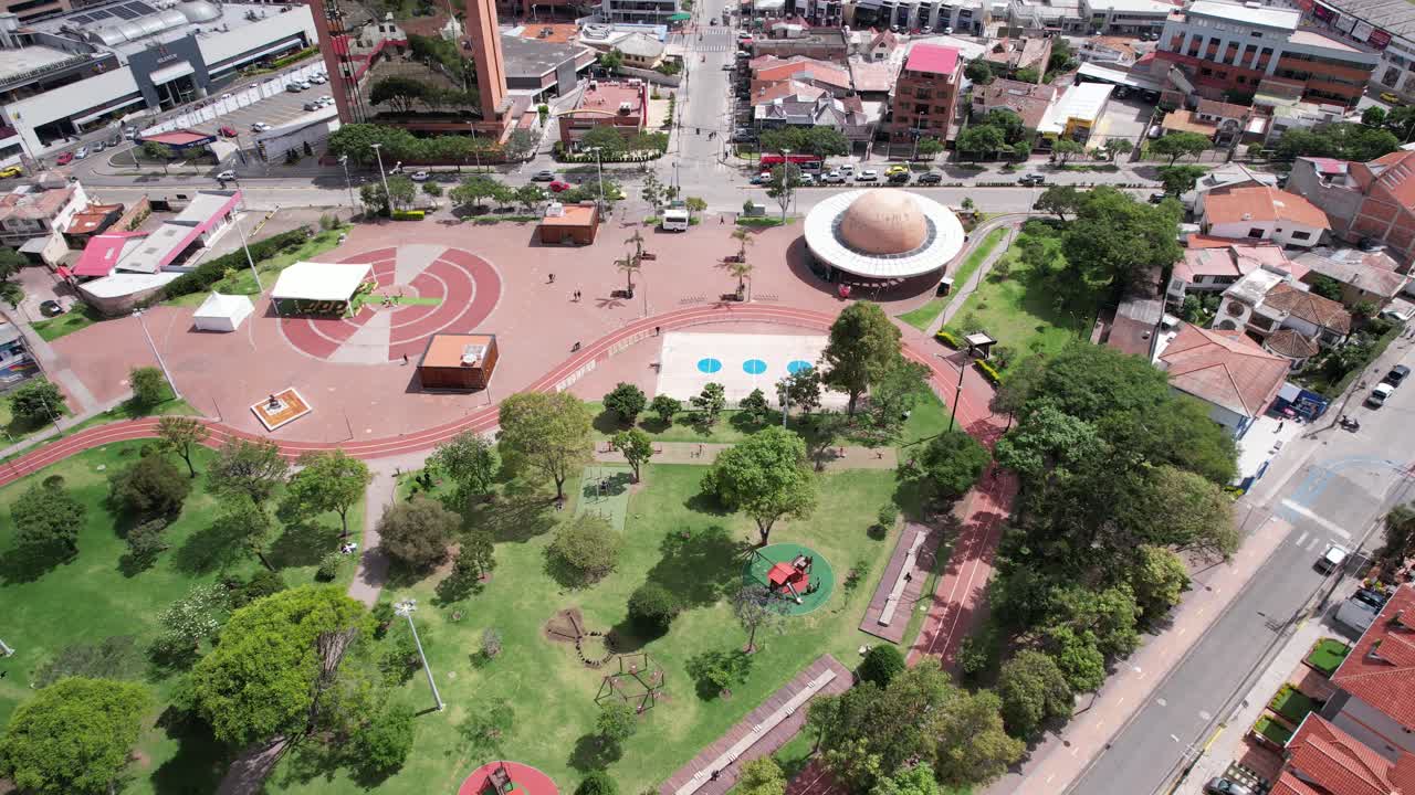 4K drone orbit over Parque de la Madre in Cuenca, Ecuador, showing the planetarium and the Cámara de Industrias surrounded by green areas and city buildings.