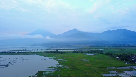 View-of-green-rice-field-on-the-side-of-lake-with-mountain-and-hill-background