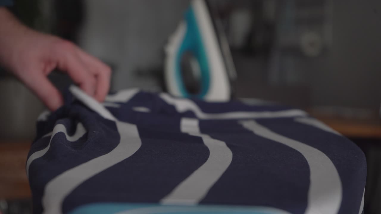 Low angle young Caucasian man irons blue stripe shirt on ironing board