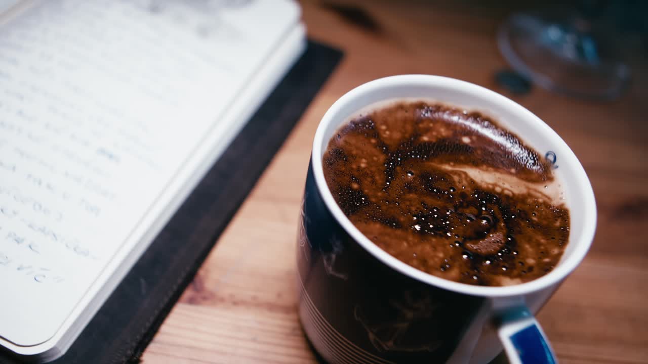 Pessoa lendo anotações de inspiração em sketchbook ao lado de café quente em mesa de madeira.