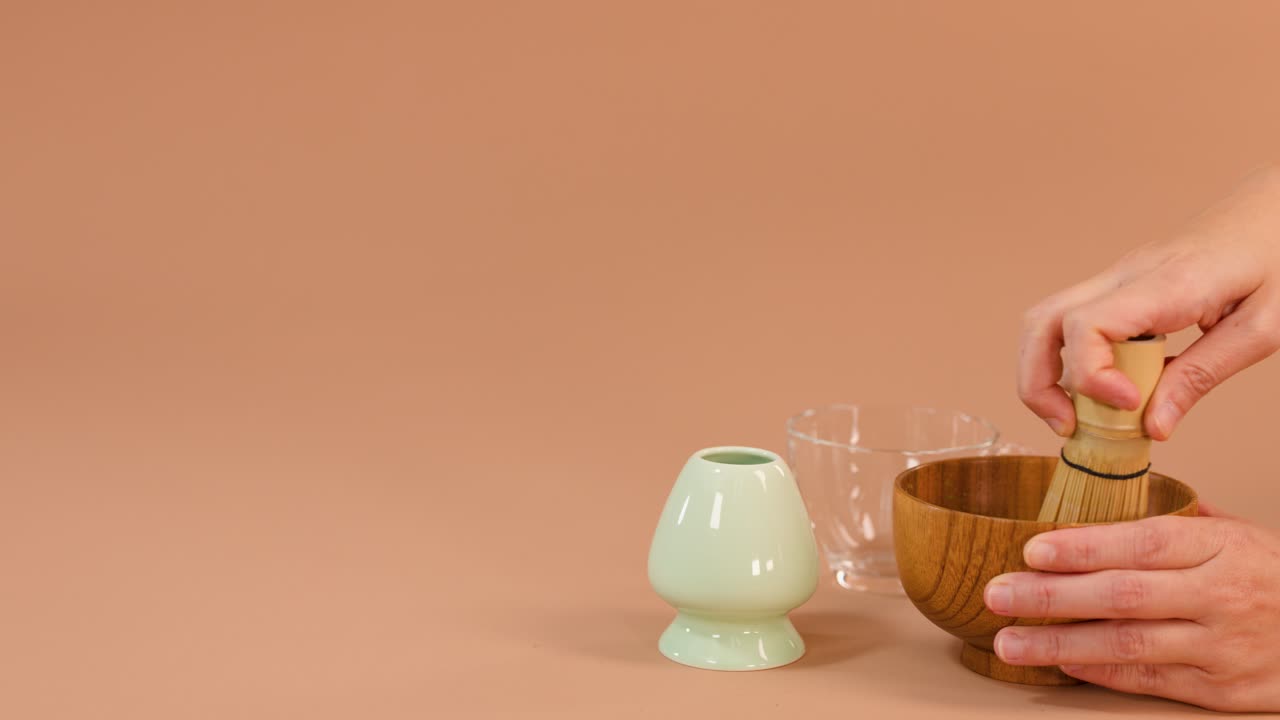 Hands whisk matcha in wooden bowl, pour into glass cup, minimal studio lighting, neutral background