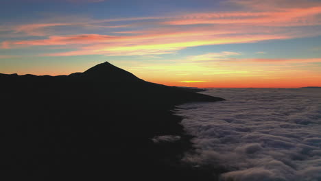 silhouette of the pico de teide mountain on canary islands against a red evening sky with a heavy cloud inversion in the valley below. pico de teide and a cloud inversion below during a red sunset 4k.