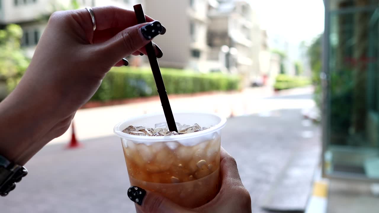 Hand stirring iced coffee with a straw.