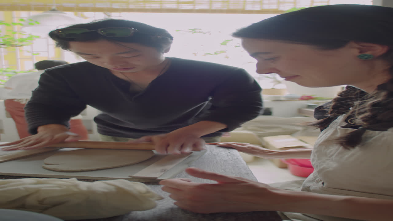 Asian Teacher Helping Female Students during Pottery Lesson