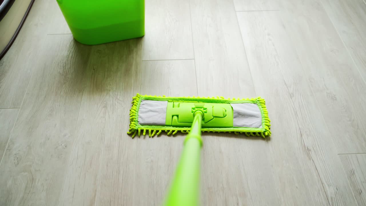Cleaning floor with water and swab. Green mop moving on the parquet floor near the green bucket with water. Daily household routine. Hygiene concept.