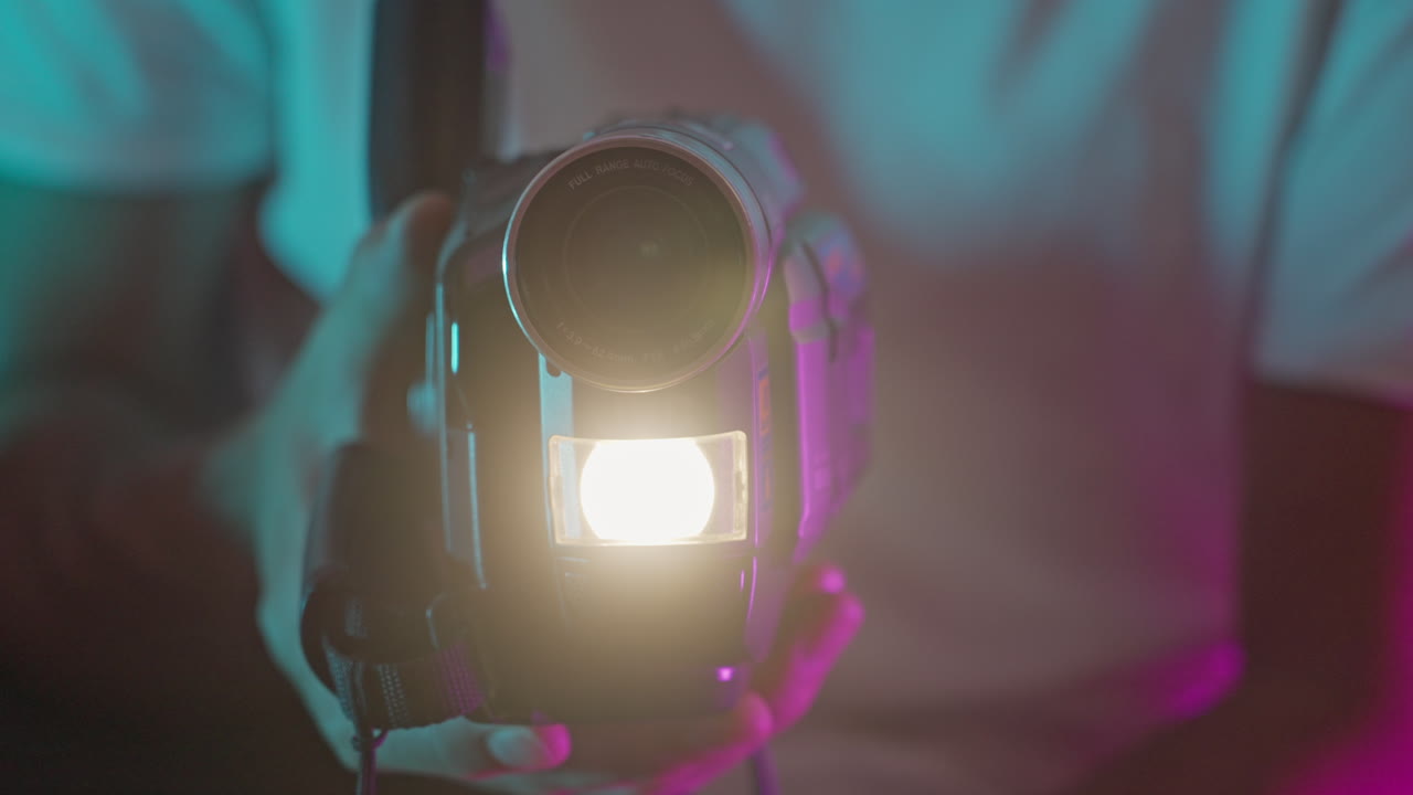 Mani che tengono una videocamera vintage con luce intensa e bokeh colorato