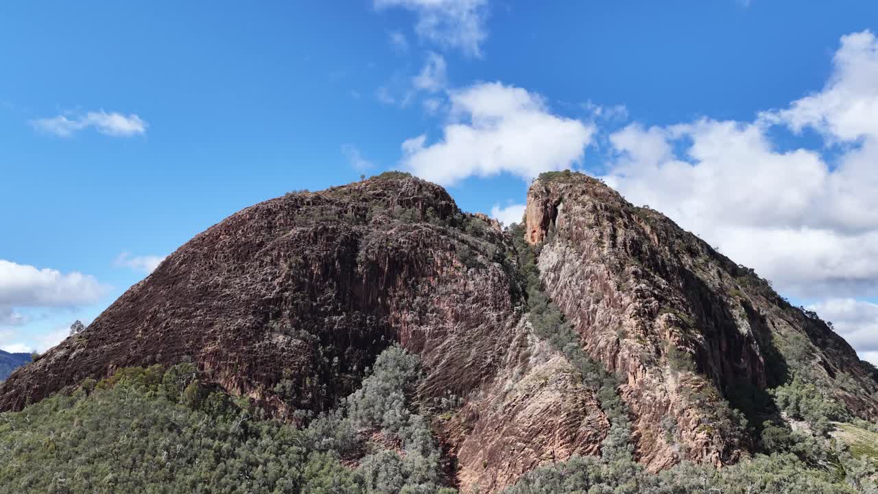 A smooth daytime camera pan reveals Split Rock’s rugged cliffs and forested slopes under clear blue skies in Warrumbungle National Park, Australia
