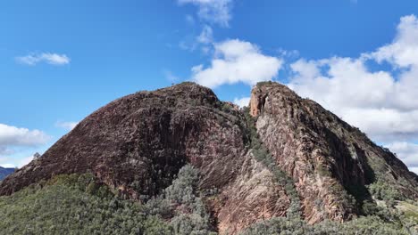 a smooth daytime camera pan reveals split rock’s rugged cliffs and forested slopes under clear blue skies in warrumbungle national park, australia