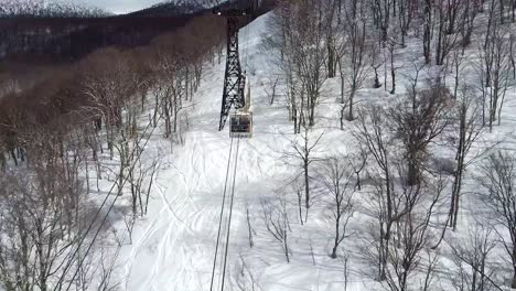 Aerial---drone-shot-of-ski-gondola-travelling-up-snowy-mountain